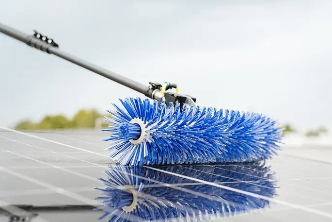 Rotierende Bürste an einer wasserführenden Stange auf einem Solarmodul, Spiegelung im Modulglas