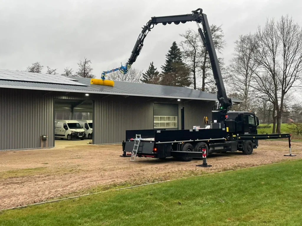 Lkw mit Bürstenkran an einer Halle